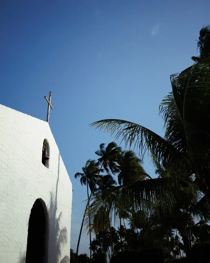 Fachada branca da Capela dos Milagres entre coqueiros